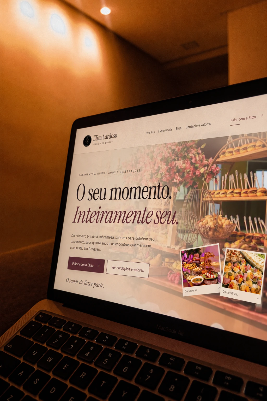 Site da Eliza Cardoso Buffet aberto num notebook, numa sala de luz âmbar.
