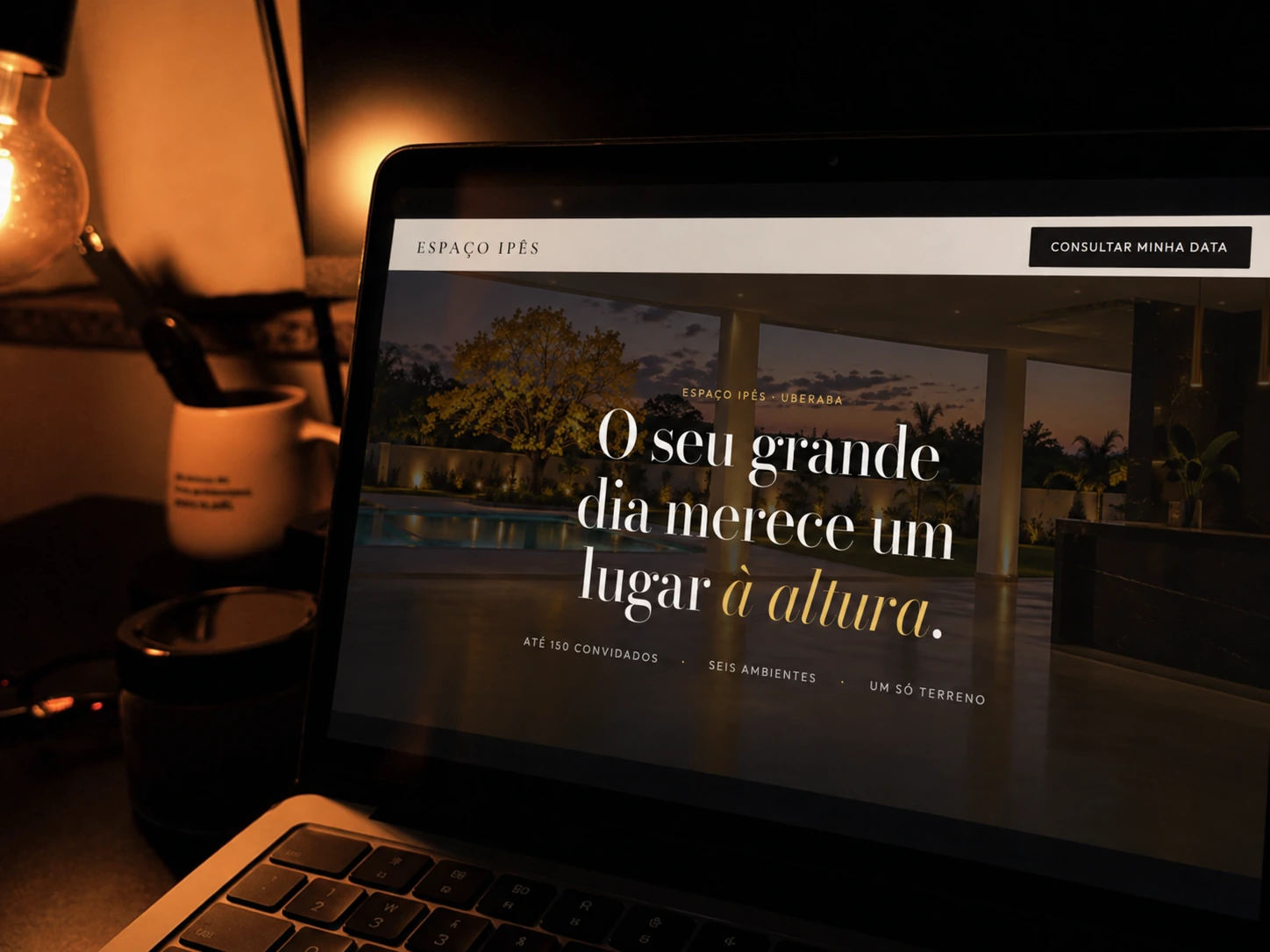 Site do Espaço Ipês aberto num notebook, à noite, ao lado de uma luminária.