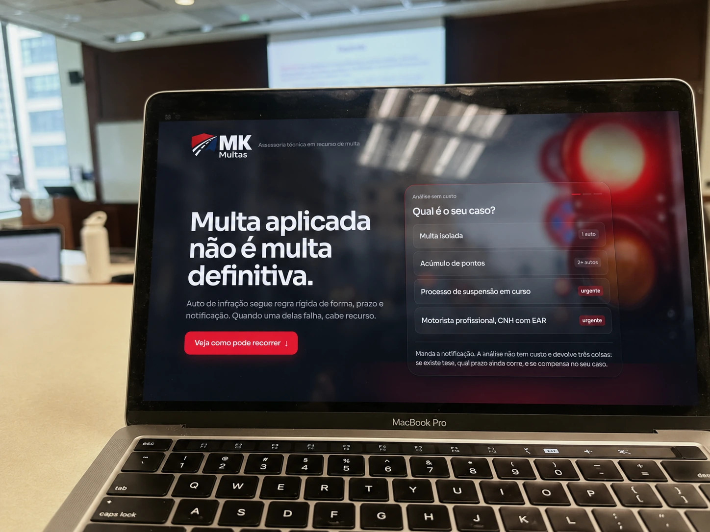 Site da MK Multas aberto num notebook, numa sala de aula de dia.