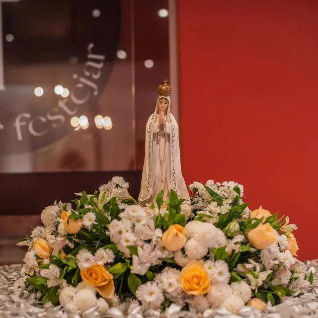 Celebração religiosa no Brindar com imagem de Nossa Senhora sobre um tapete de flores brancas e amarelas.