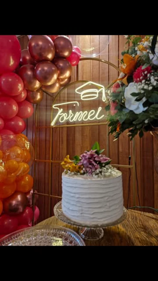 Formatura no Brindar: bolo branco, letreiro de neon Formei e balões dourados.